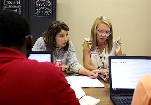 Two students study on a laptop at a crowded table